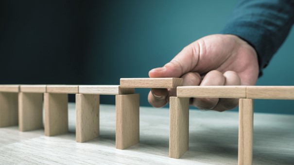 Auf dem Bild ist eine Brücke aus Holzspielklötzen zu sehen. Eine Han schließt eine vorhandene Lücke mit einem weiteren Holzklötzchen.