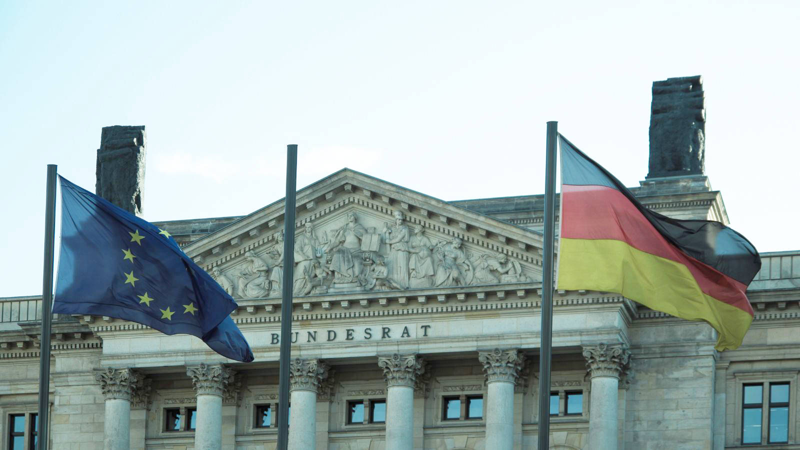 Das Bild zeigt das Gebäude des Bundesrats von außen mit einer wehenden Deutschland- und einer EU-Flagge.
