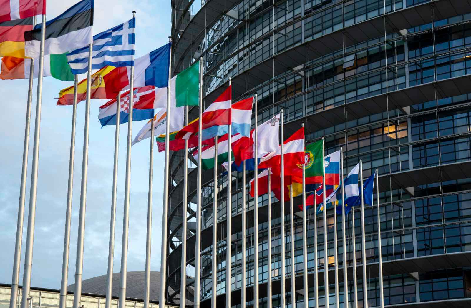 Das Foto zeigt die Flaggen verschiedener EU-Mitgliedsstaaten, die an Flaggenmasten vor einem Gebäude aufgehängt sind..